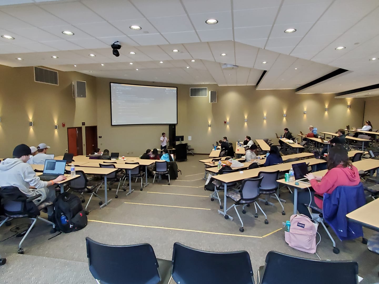 A Python workshop at HackBU 2023: students at tables around a wide room, facing a projector screen.