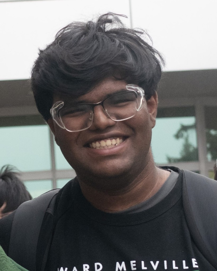 Portrait of Aditya Kumar, HackBU organizer, grinning in clear-framed glasses outside a campus building.