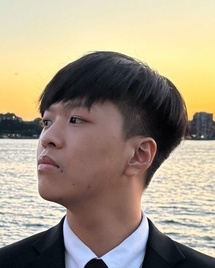 Portrait of Daniel Zheng, HackBU Vice President of Software, in profile in a dark suit and tie beside a river at sunset.