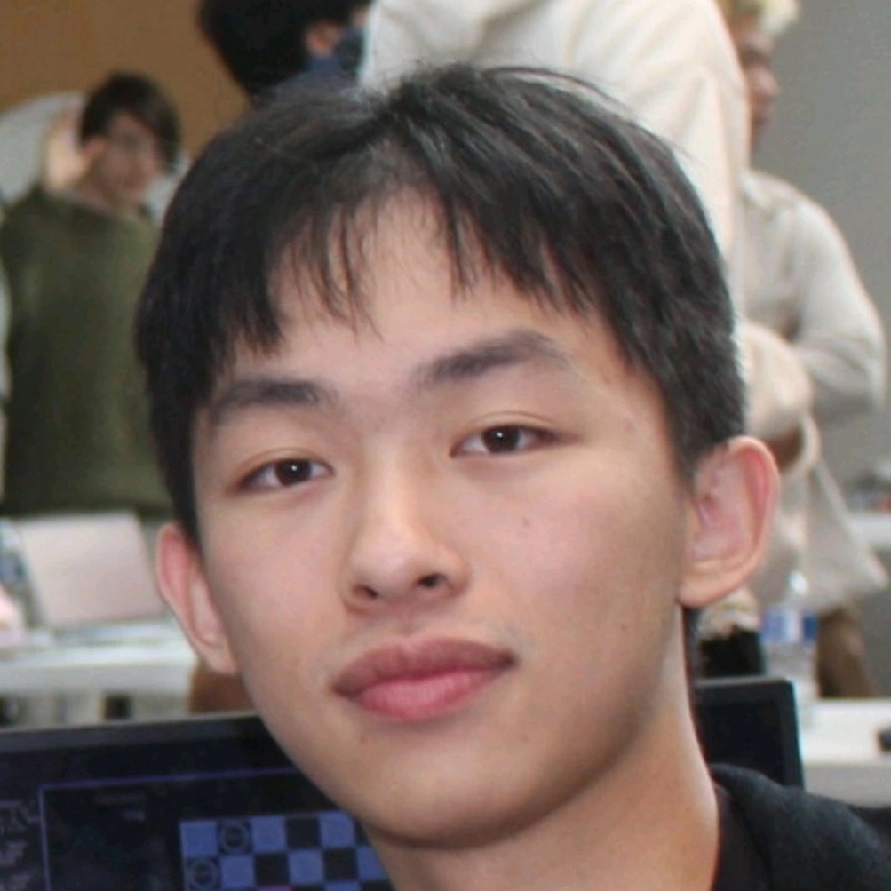 Portrait of Hewitt Wang, HackBU organizer, close-up at a busy hackathon with a laptop in front of him.