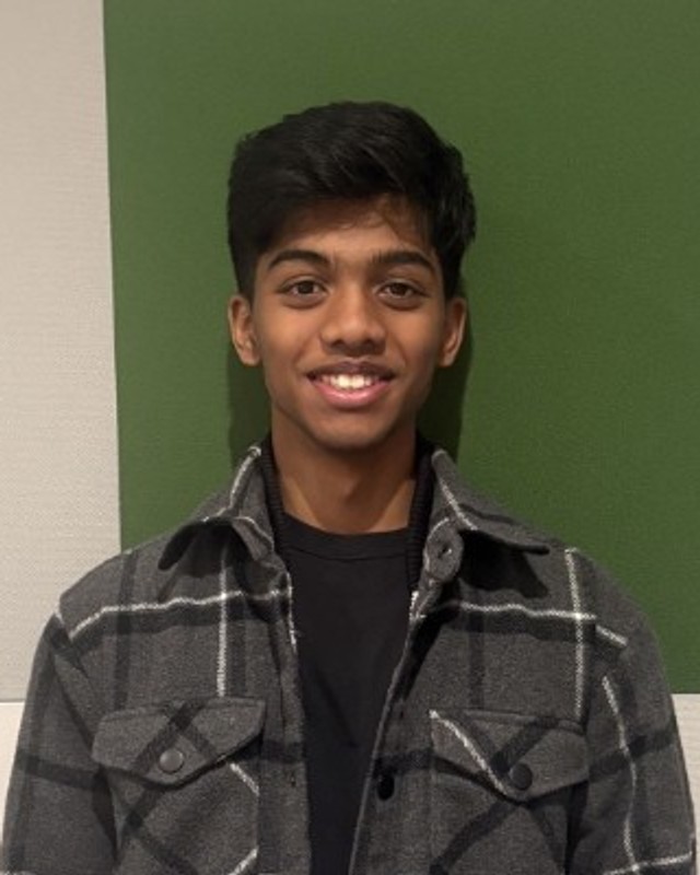Portrait of Joshuanaveen Navaneetharaja, HackBU organizer, smiling in a gray plaid shirt jacket against a green wall panel.