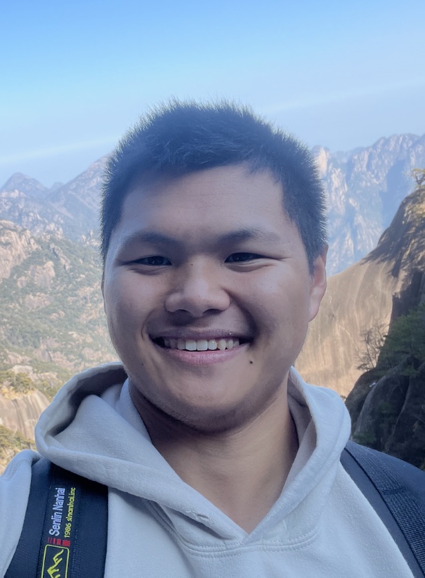 Portrait of Samuel Yu, HackBU Vice President of Communications, grinning in a gray hoodie in front of rocky mountain peaks.