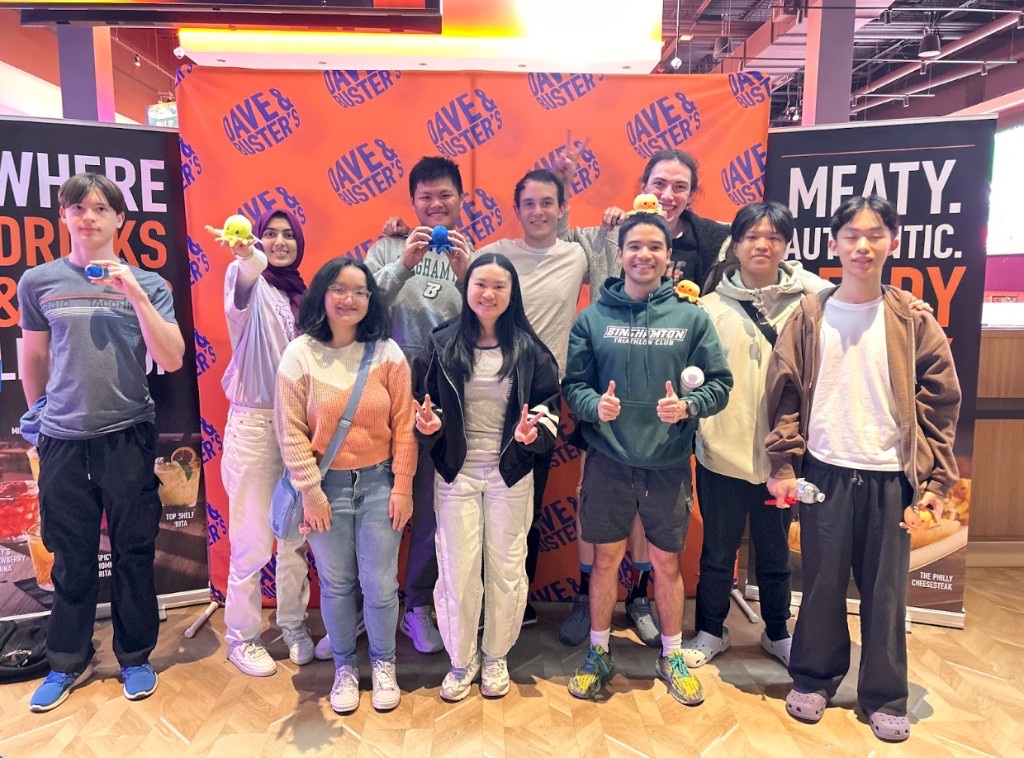 HackBU organizers posing together at a group outing, standing in front of an orange backdrop.